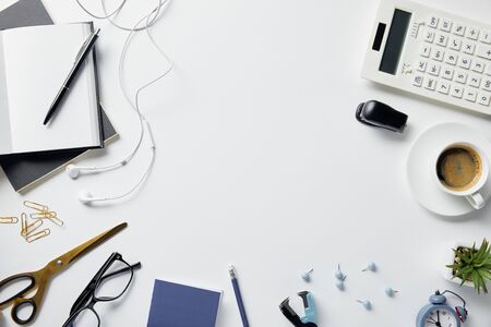 top view of plant, glasses, coffee, earphones and office supplies on white surface