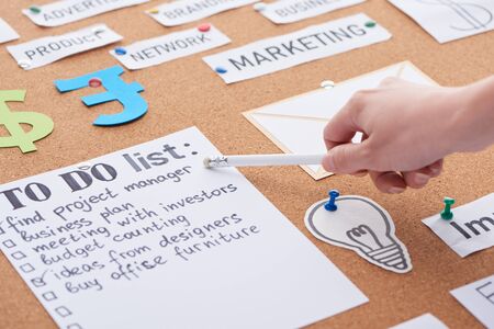 cropped view of woman pointing with pencil on to do list on cork board