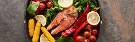 top view of uncooked salmon steak with vegetables, lemon and herbs in grill pan, panoramic shot