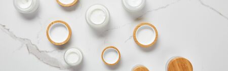panoramic shot of jars with cosmetic cream and wooden caps on white surface
