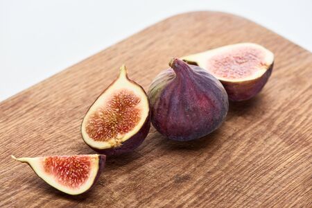 ripe whole and cut delicious figs on wooden chopping board isolated on white