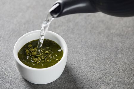 black kettle pouring water in white cup with green matcha powderの写真素材