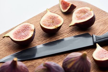 ripe whole and cut delicious figs on wooden chopping board with knife isolated on white