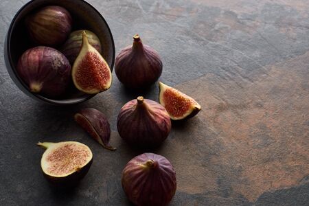 ripe whole and cut delicious figs scattered from bowl on stone backgroundの写真素材