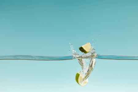 ripe lime halves falling deep in water with splashes on blue backgroundの写真素材