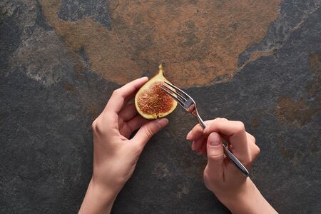 cropped view of woman holding fork and ripe delicious fig half on stone backgroundの写真素材