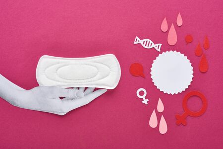 top view of paper cut white hand with white sanitary napkin near blood drops and female signs on purple backgroundの写真素材