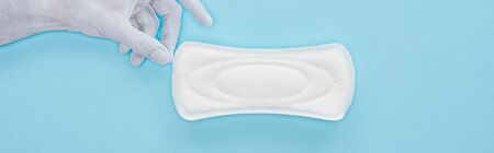 top view of white paper hand holding cotton sanitary towel on blue background, panoramic shot