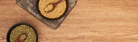 panoramic shot of black bowls with grains and maash beans with spoons on wooden cutting board