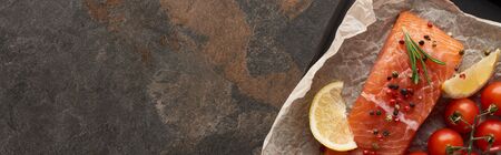 panoramic shot of raw salmon steak with tomatoes, rosemary, lemon and pepper on bakery paper on oven trayの写真素材