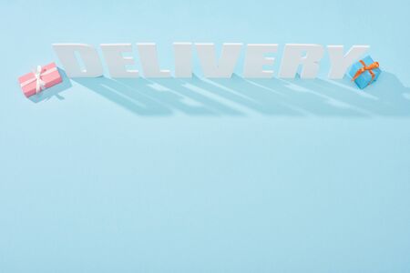 top view of white delivery inscription with shadows near gift boxes on blue backgroundの写真素材