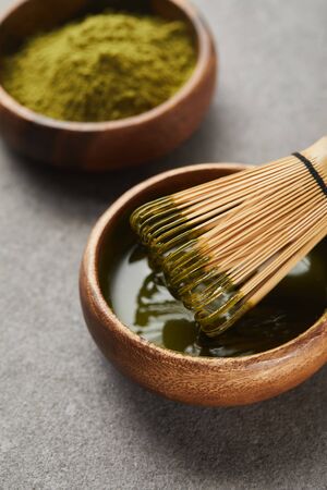 selective focus of green matcha powder and bamboo whisk in wooden bowl with teaの写真素材