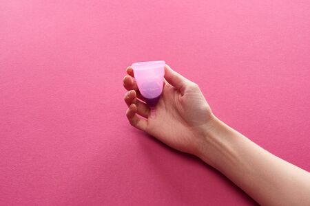 partial view of woman holding plastic menstrual cup with blood on purple backgroundの写真素材
