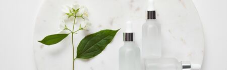 panoramic shot of plate with jasmine and cosmetic glass bottles on white surfaceの写真素材