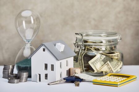 house model on white table with hourglass, calculator, money and keys, real estate concept