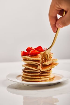 cropped view of man taking slice of pancakes with strawberries on white plate isolated on greyの写真素材