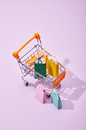 few small paper bags near toy cart with colorful shopping bags on violet backgroundの写真素材