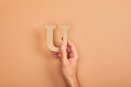 cropped view of man holding paper cut letter U on beige backgroundの写真素材