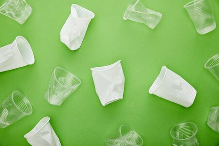 top view of disposable white and transparent plastic cups on green backgroundの写真素材