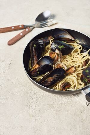delicious pasta with seafood in frying pan near cutlery on textured grey backgroundの写真素材