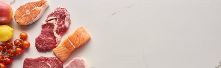 Panoramic shot of raw meat, fish and poultry near tomatoes, lemon and apple on marble surface with copy spaceの写真素材