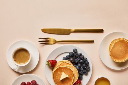 top view of tasty served breakfast with pancakes, berries, honey and coffee near golden cutleryの写真素材