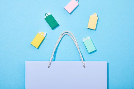 top view of colorful paper bags falling into purple shopping bag on blue
