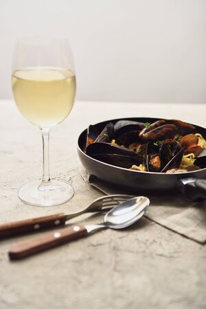 tasty Italian pasta with seafood served in frying pan with white wine, napkin and cutlery isolated on greyの写真素材