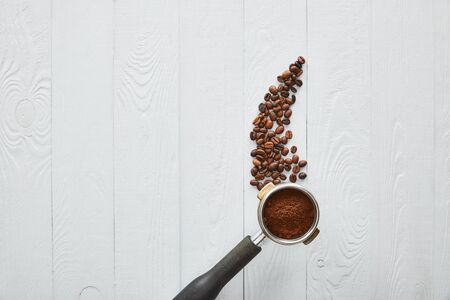 Top view of portafilter with coffee on white wooden surface with coffee beansの写真素材