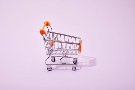decorative toy shopping cart with orange handle on violet backgroundの写真素材