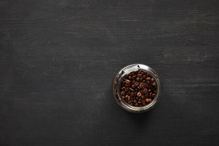Glass jar with coffee beans on dark wooden surfaceの写真素材