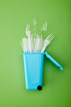 top view of blue recycle bin with broken plastic forks and straws on green background