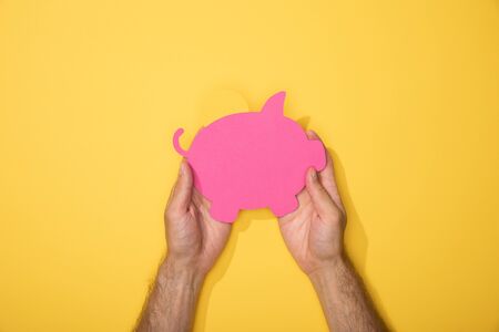 cropped view of man holding pink paper piggy bank on yellowの写真素材