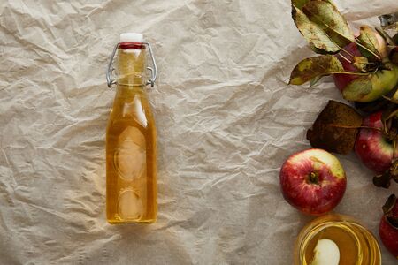 top view of parchment paper with fresh apples, bottle and glass of cider with copy space