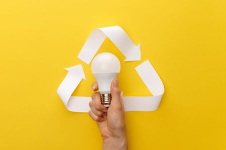 cropped view of woman holding light bulb under paper craft triangle on yellow background