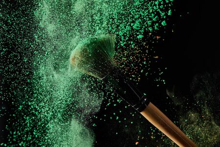 cosmetic brush with green powder explosion on black background