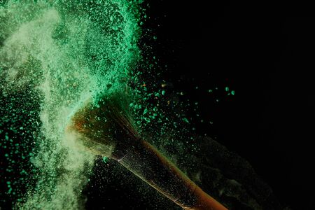 soft cosmetic brush with colorful green powder explosion on black backgroundの写真素材