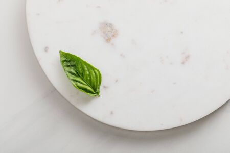 Top view of round marble surface with green basil leaf on white backgroundの写真素材