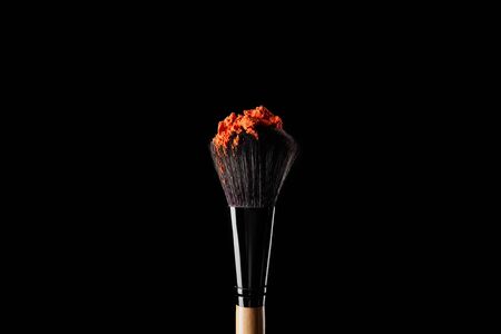 cosmetic brush with colorful orange powder isolated on black