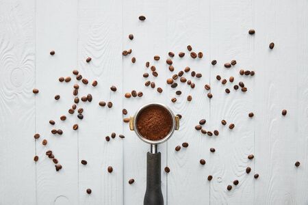 Top view of portafilter with coffee on white wooden surface with scattered coffee beansの写真素材