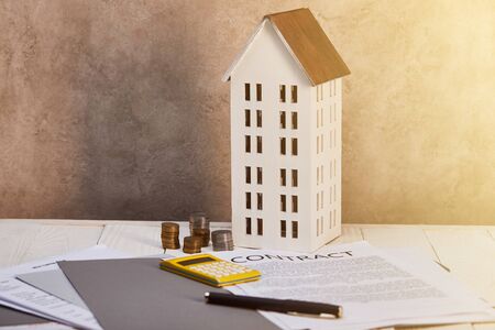 house model near coins, calculator, pen and contract on table with sunlight, real estate conceptの写真素材