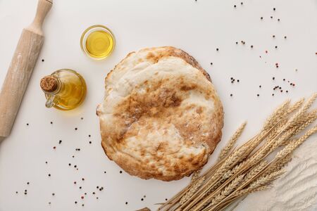 top view of lavash bread near spikes and olive oil on white surface with peppercornsの写真素材