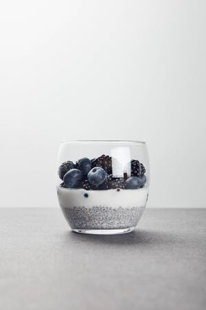 tasty yogurt with chia seeds, blueberries and blackberries on marble surface isolated on greyの写真素材
