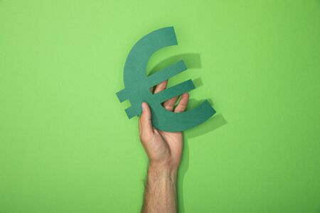 cropped view of man holding euro currency sign on greenの写真素材