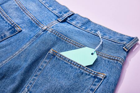 close up view of turquoise paper sale tag on rope on jeans on violetの写真素材