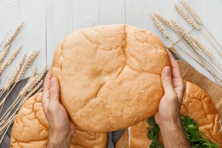 cropped view of man holding lavash bread above white wooden surface