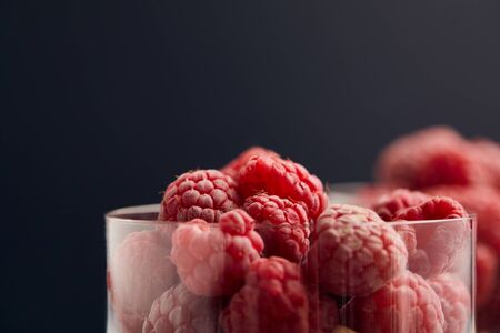 selective focus of fresh raspberries in glasses isolated on blackの写真素材