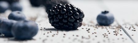 panoramic shot of scattered blackberries, blueberries and chia seeds on white wooden table isolated on blackの写真素材