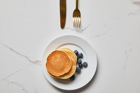 top view of pancakes with blueberries on plate near golden fork and knifeの写真素材