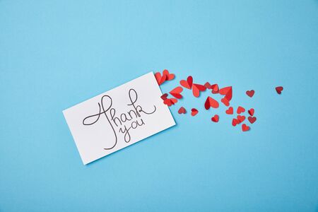 white card with thank you lettering and red paper hearts on blue backgroundの写真素材